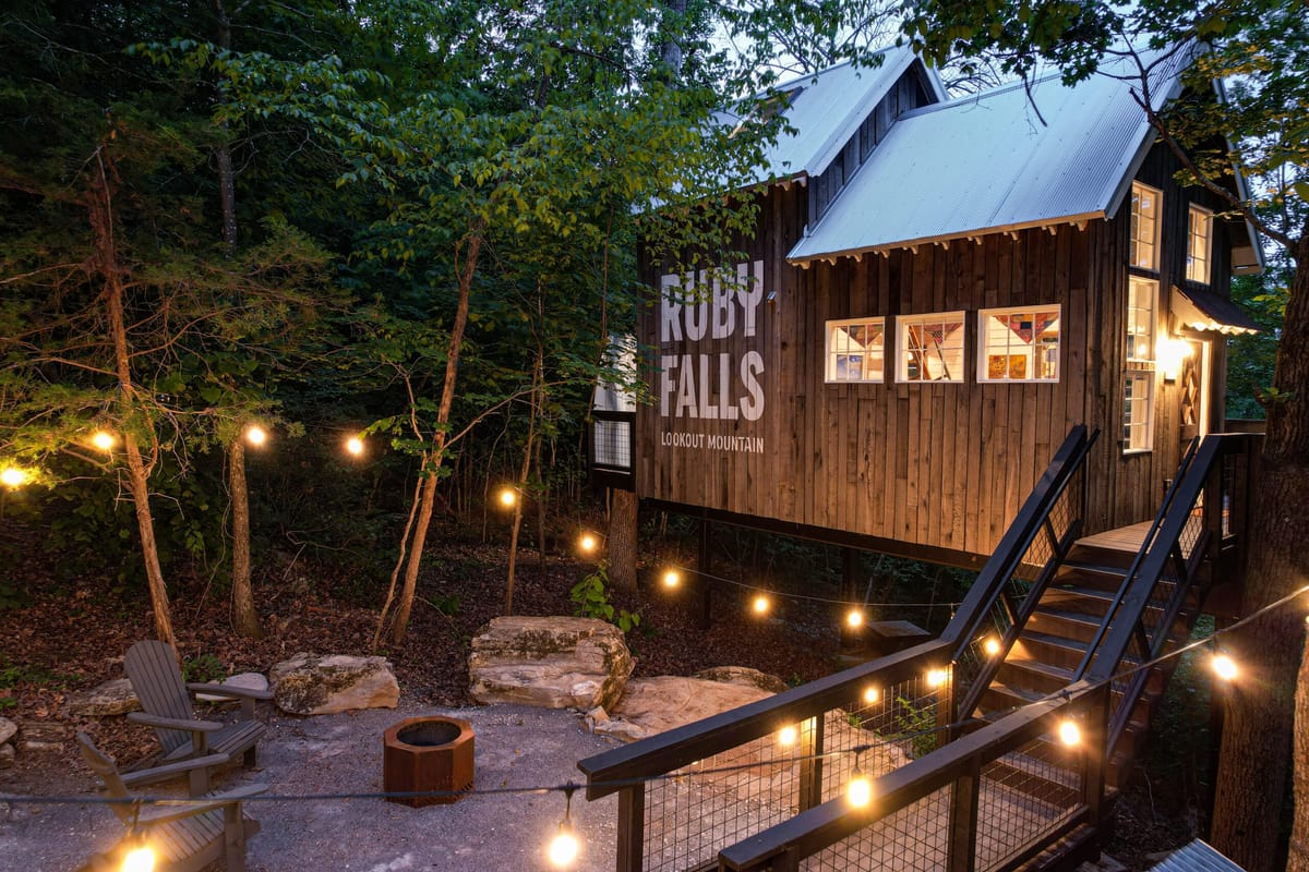 Treetop Hideaways treehouse at night showing a firepit and strings of cafe lights illuminating a hand painted Ruby Falls sign on the side of the treehouse.
